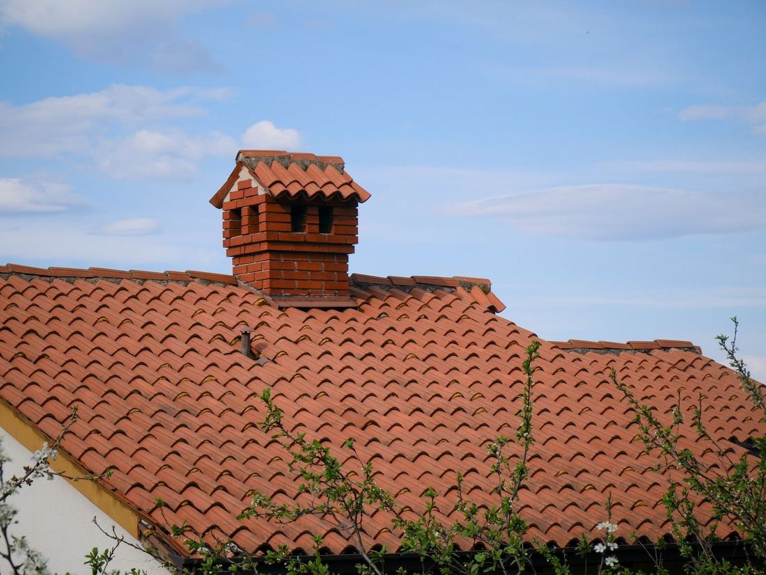 Stary dach z dachówki ceramicznej z mchem i kominem w wiosennym świetle